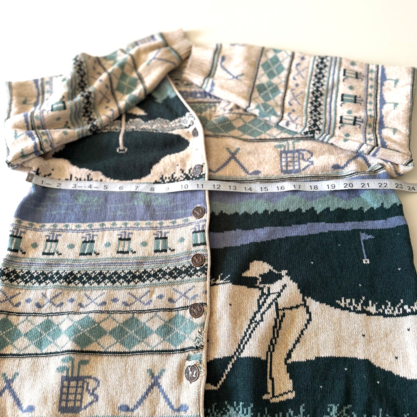 Golf themed cardigan with a white backdrop with a measuring tape on it. 