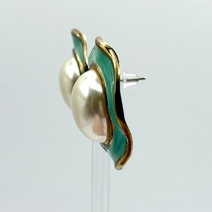 Pair of earrings with gold and green design on a clear stand against a light gray background