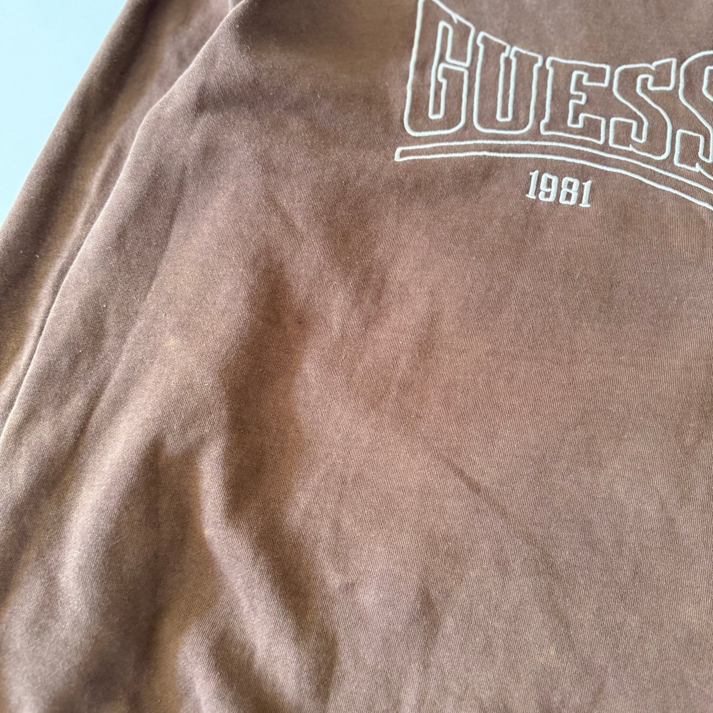 Brown fabric with Guess logo and '1981' text on a light blue background