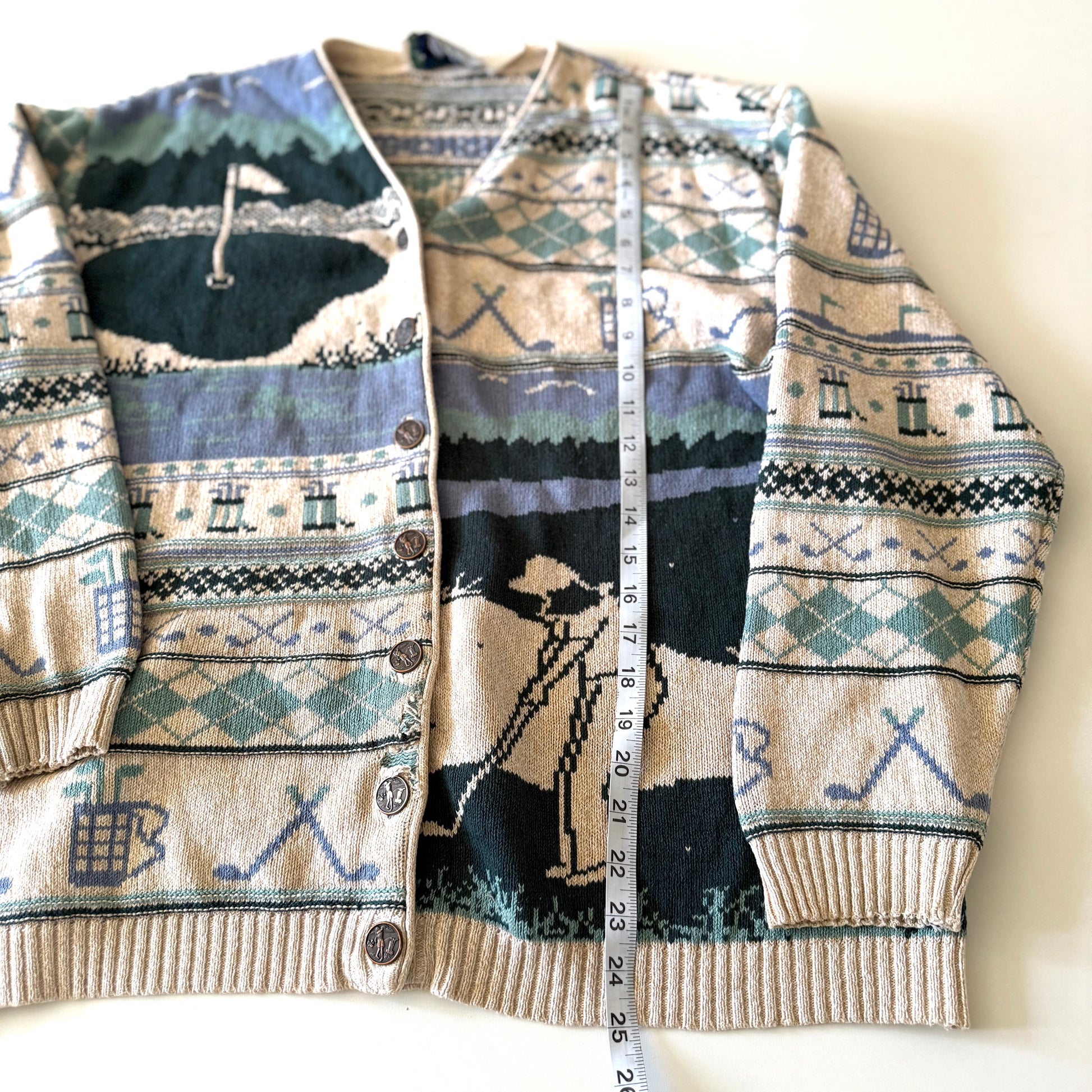 Golf themed cardigan with a white backdrop with a measuring tape on it. 