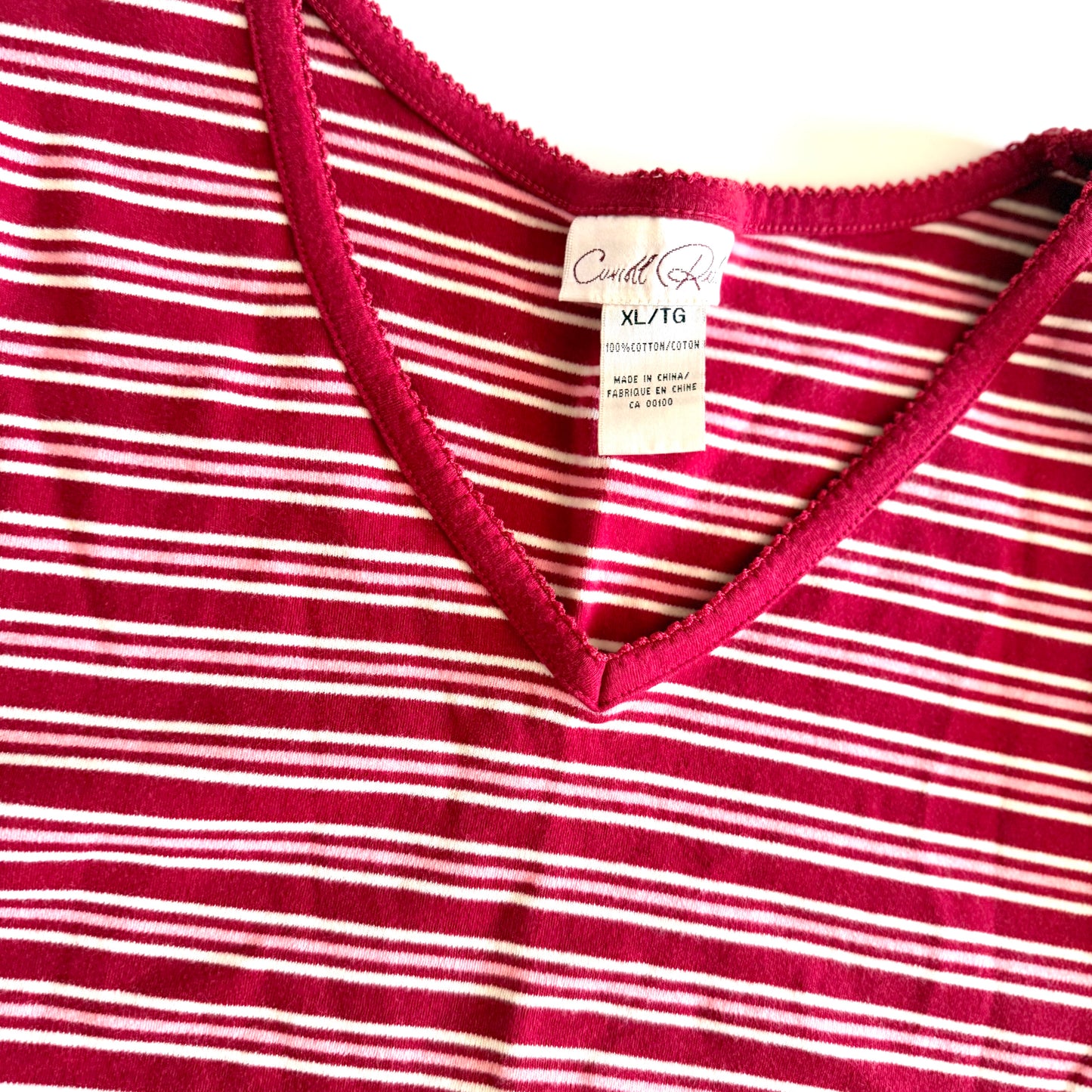 White, pink, and red striped t-shirt with a v-neck collar on a white backdrop. 
