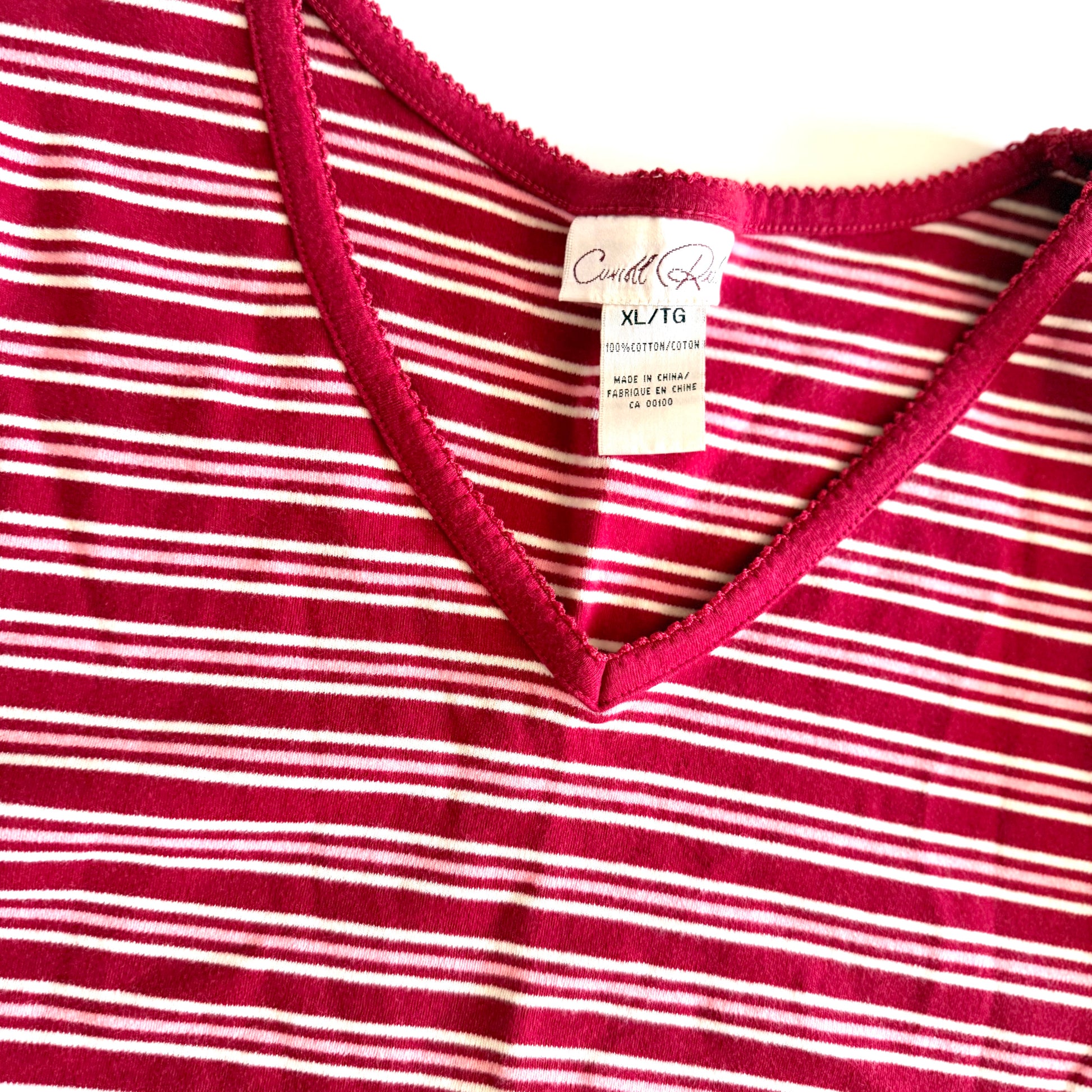 White, pink, and red striped t-shirt with a v-neck collar on a white backdrop. 