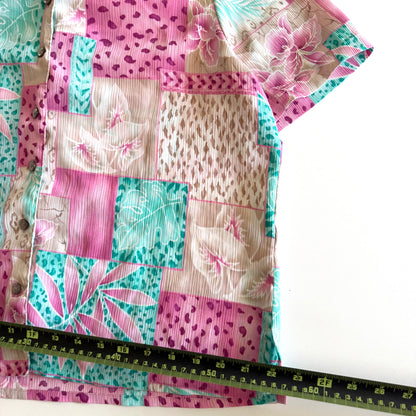 Button down bright coloured (tan, pink, teal) shirt with tropical and animal print patterns on it - placed on a white background with a measuring tape on it. 