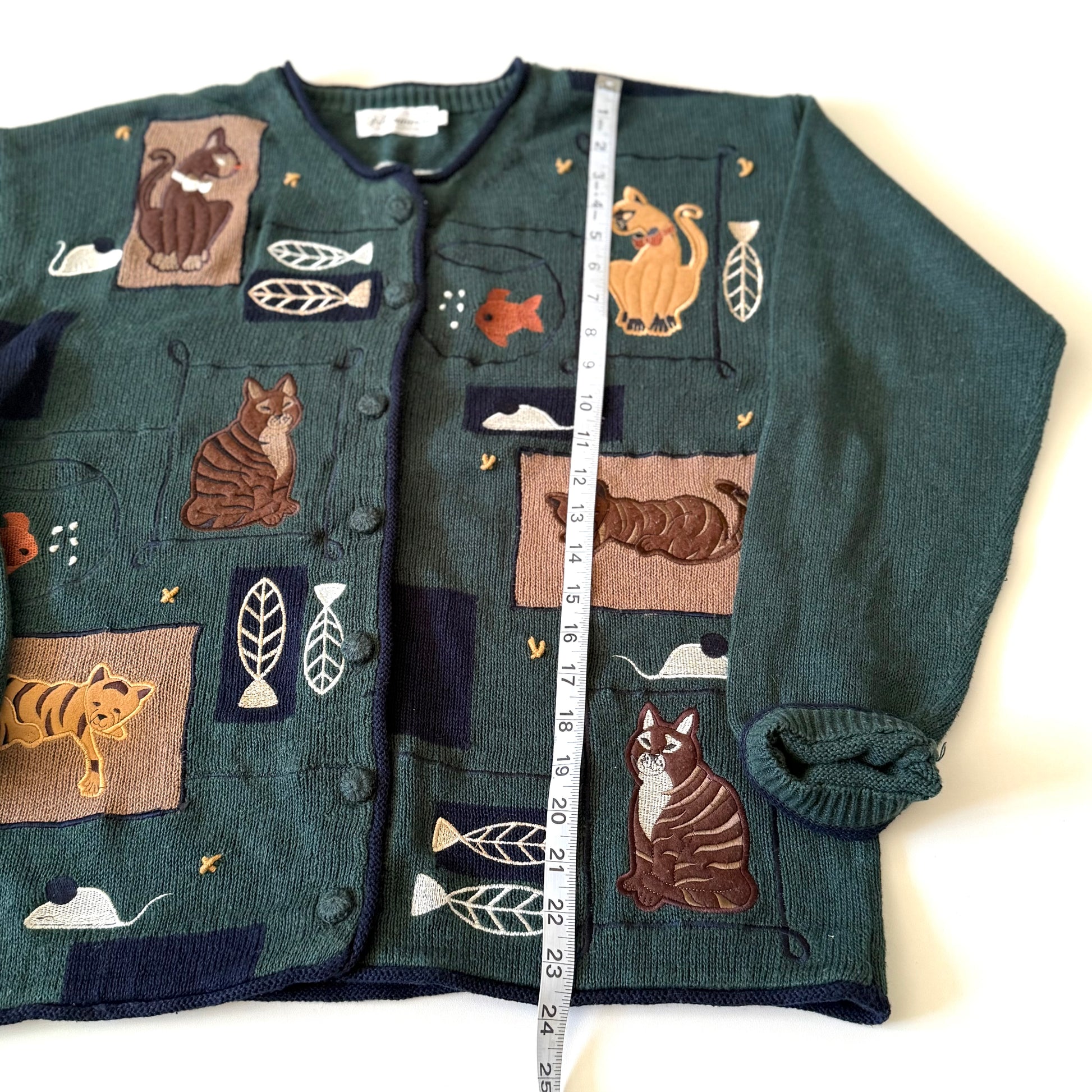 Green cardigan with cat-themed patches on a white background