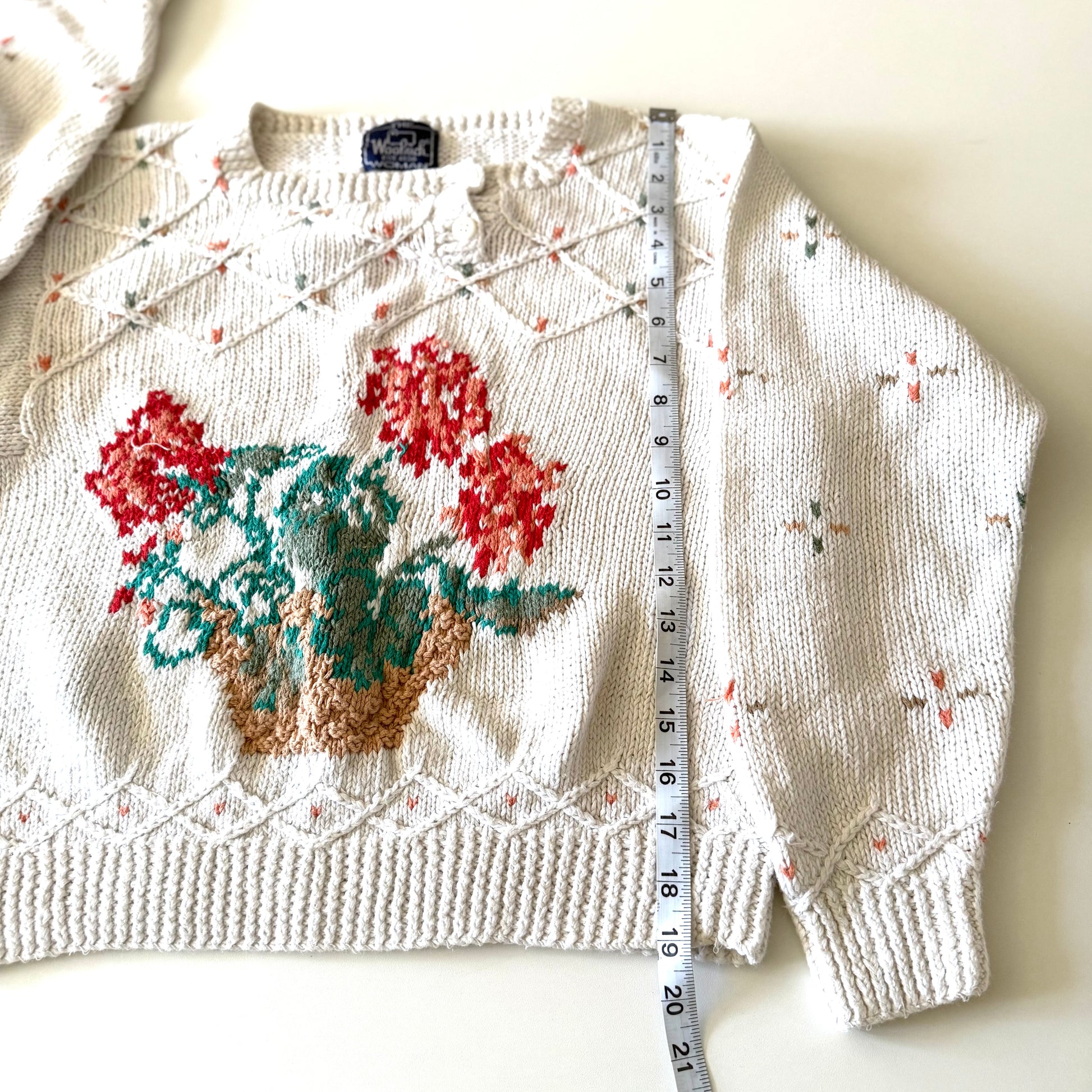 Knitted sweater with floral design and a measuring tape for size reference on a white background