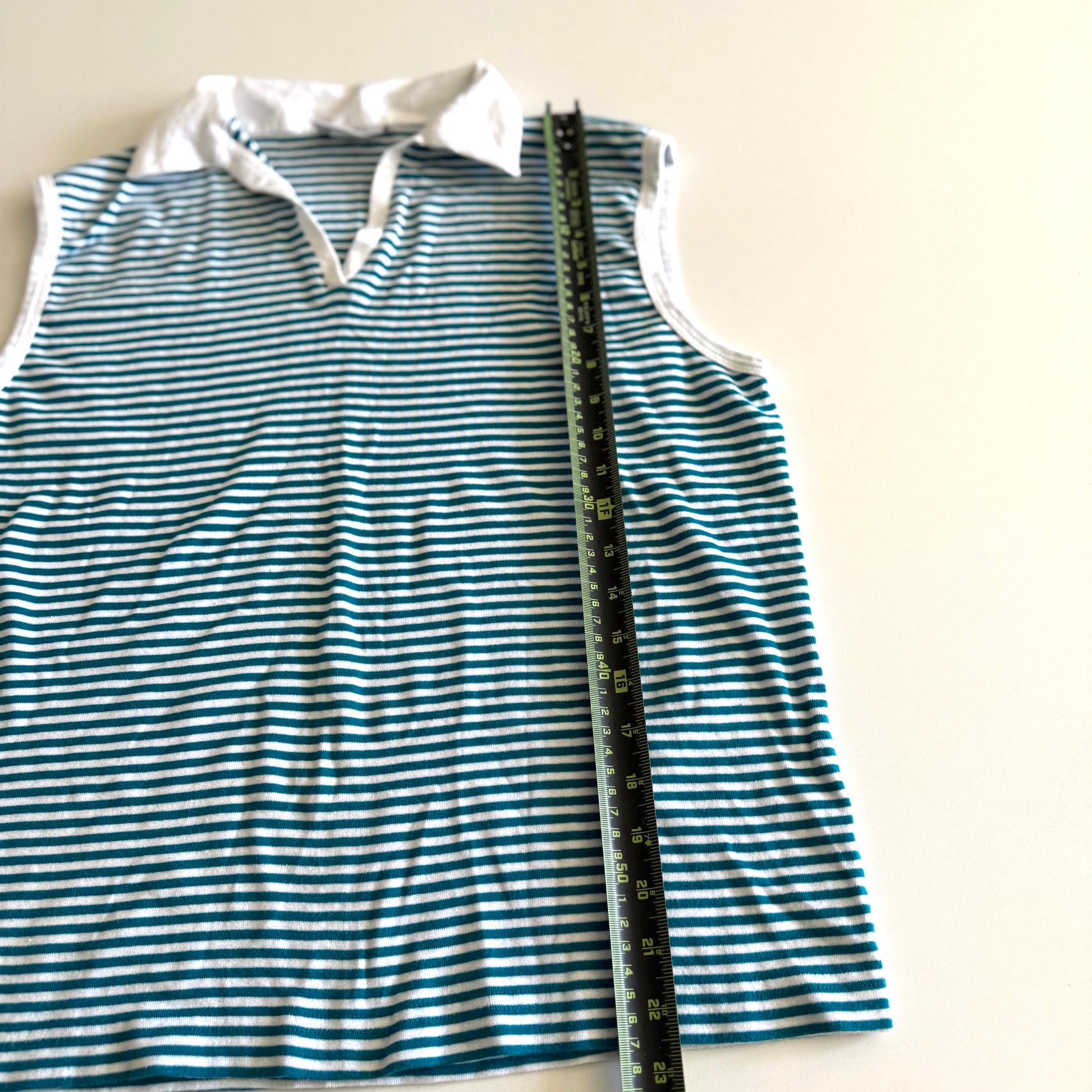 White and turquoise striped tank top with polo neckline, on a white backdrop and a measuring tape laid on top of it. 