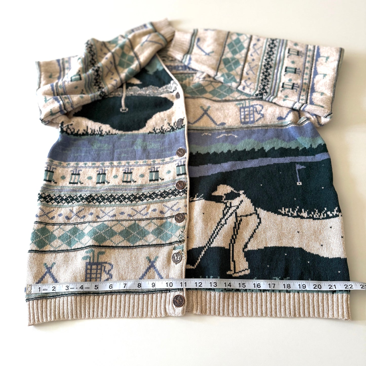 Golf themed cardigan with a white backdrop with a measuring tape on it. 