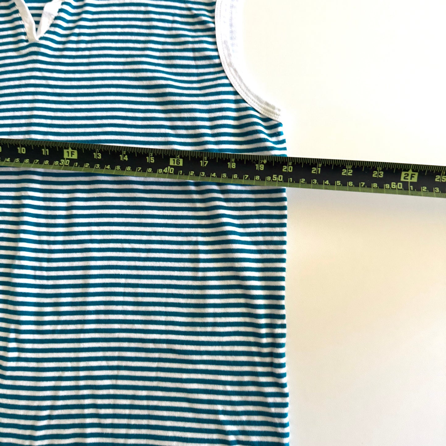 White and turquoise striped tank top with polo neckline, on a white backdrop and a measuring tape laid on top of it. 
