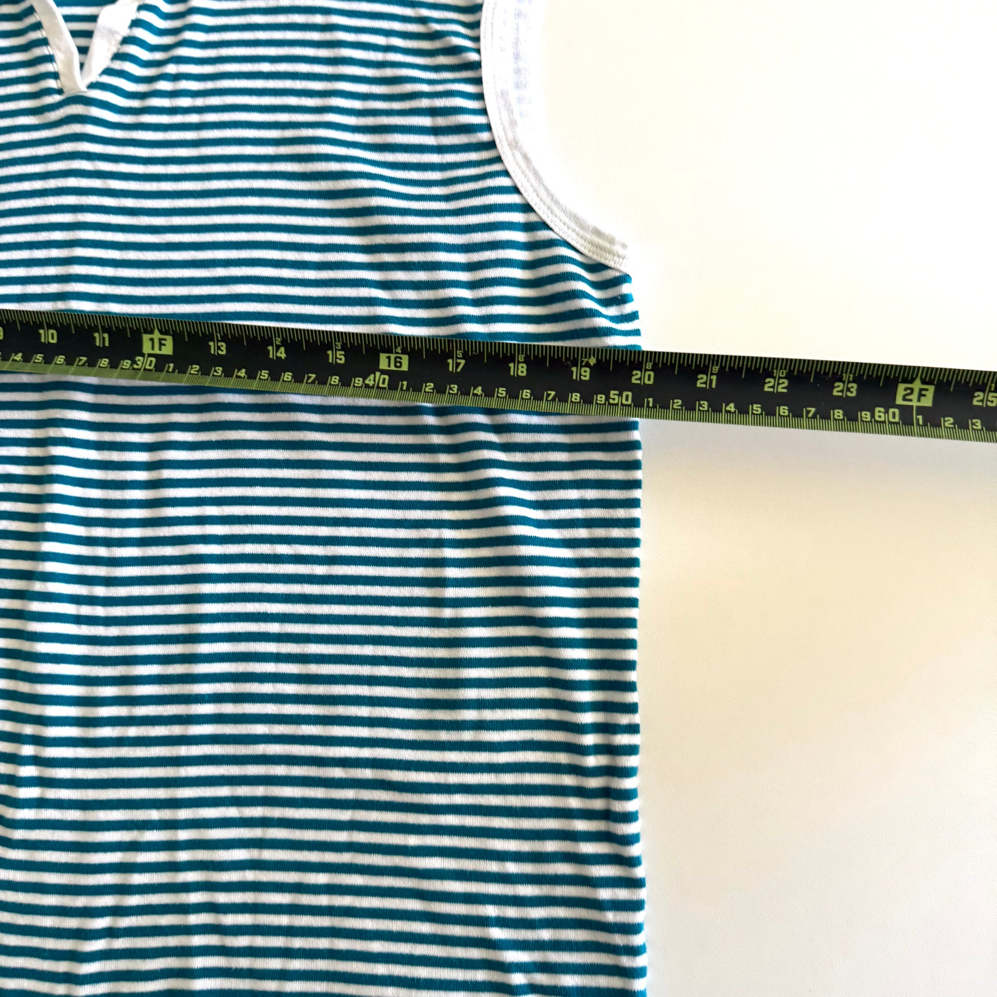 White and turquoise striped tank top with polo neckline, on a white backdrop and a measuring tape laid on top of it. 
