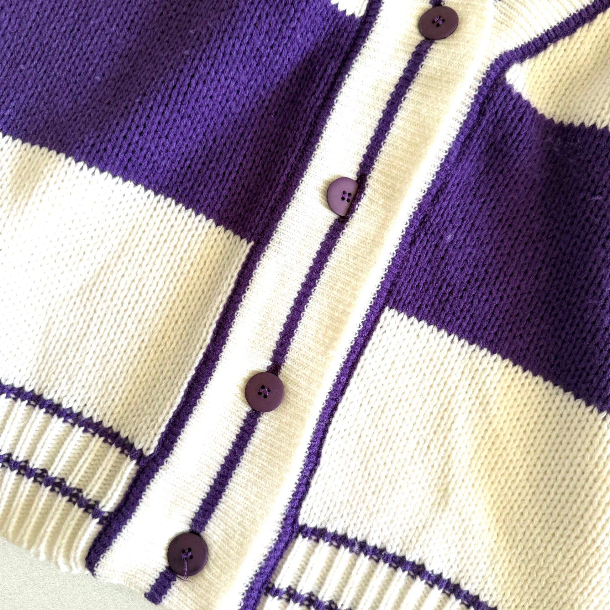 Close up of buttons on a purple and white striped cardigan. 