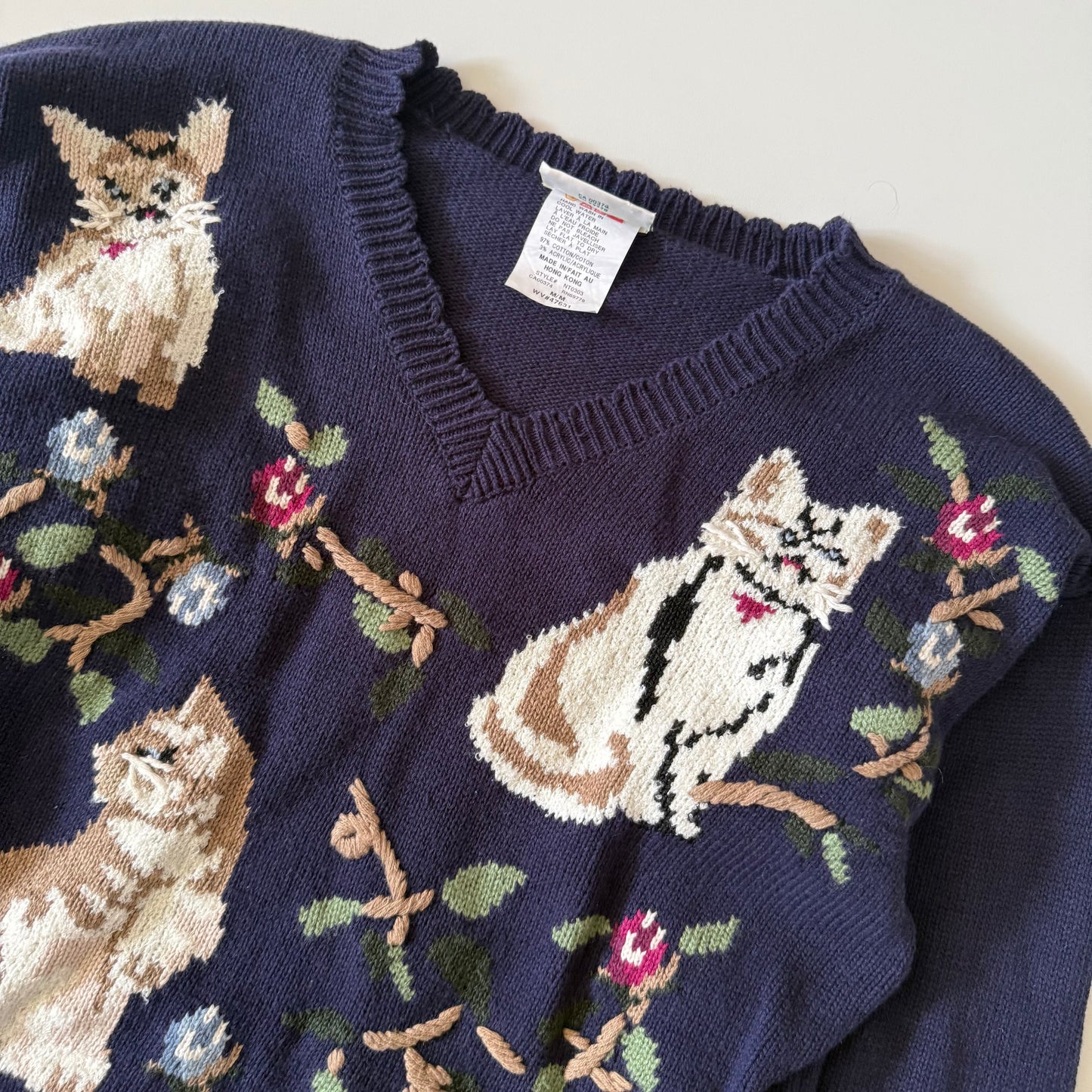 Navy blue sweater with cat and floral patterns on a white background