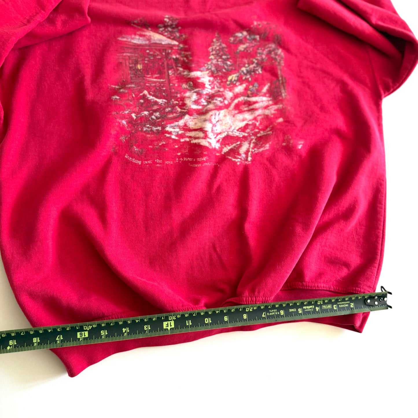 Bold pink sweatshirt / crewneck with a winter scene on the front  laid on a white backdrop - with a measuring tape laid out on it. 