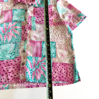 Button down bright coloured (tan, pink, teal) shirt with tropical and animal print patterns on it - placed on a white background with a measuring tape on it. 