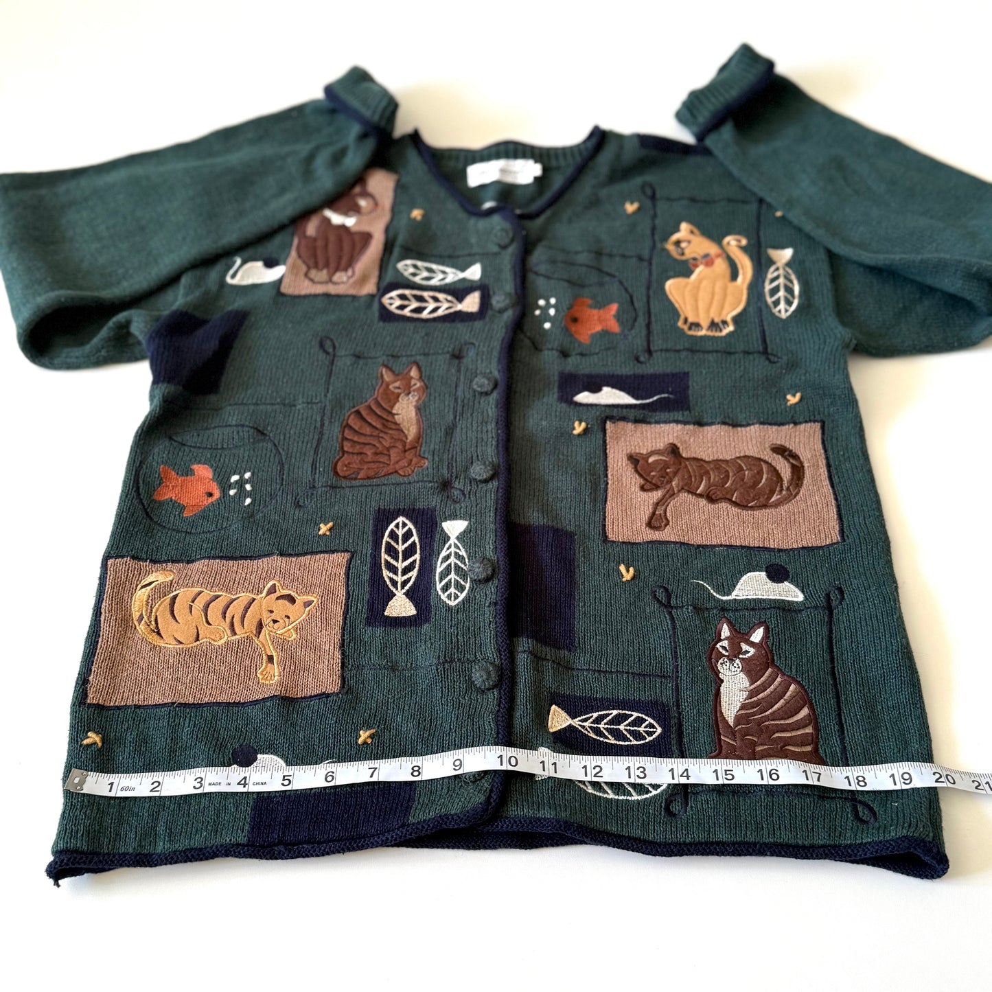 Green sweater with embroidered animal designs on a white background