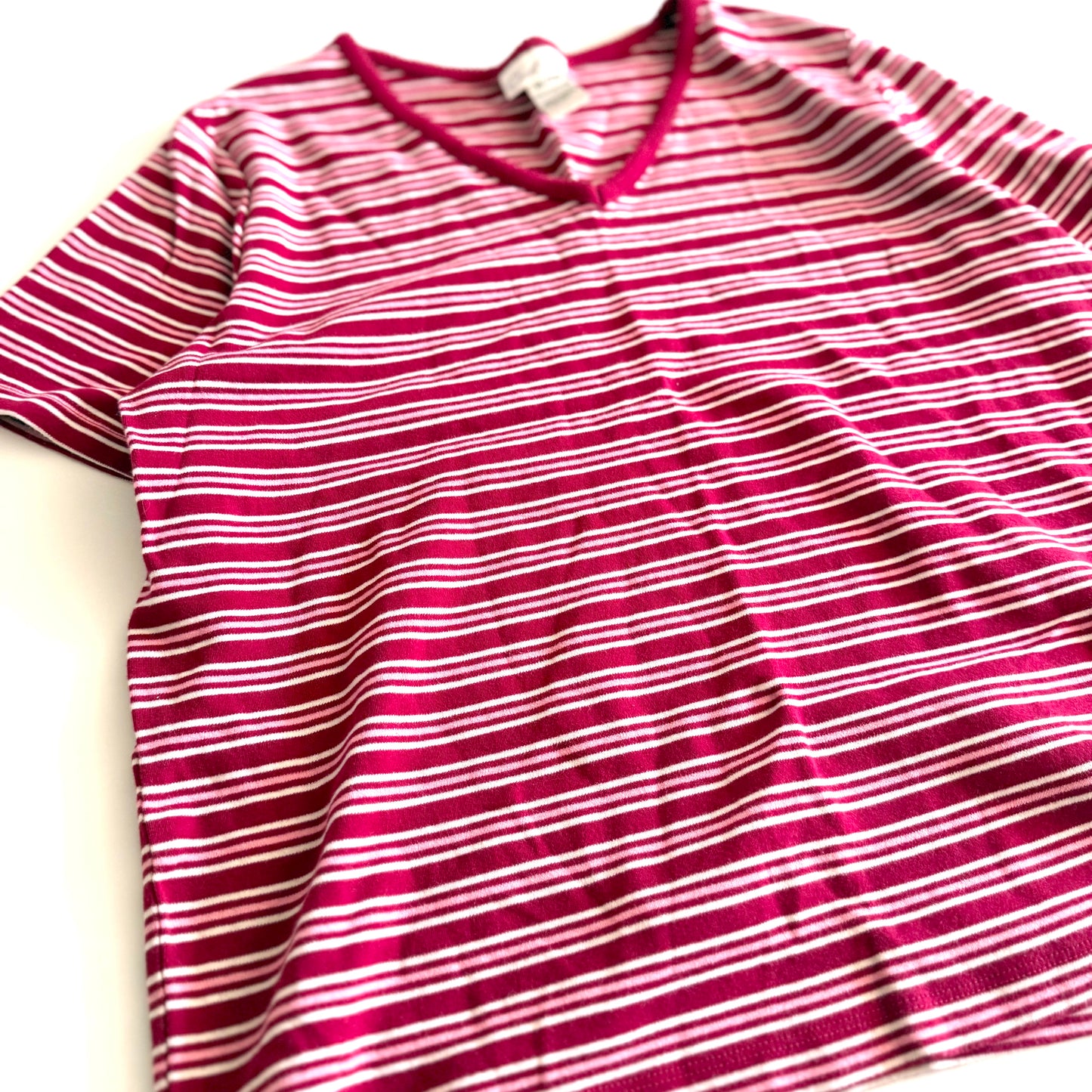 White, pink, and red striped t-shirt with a v-neck collar on a white backdrop. 