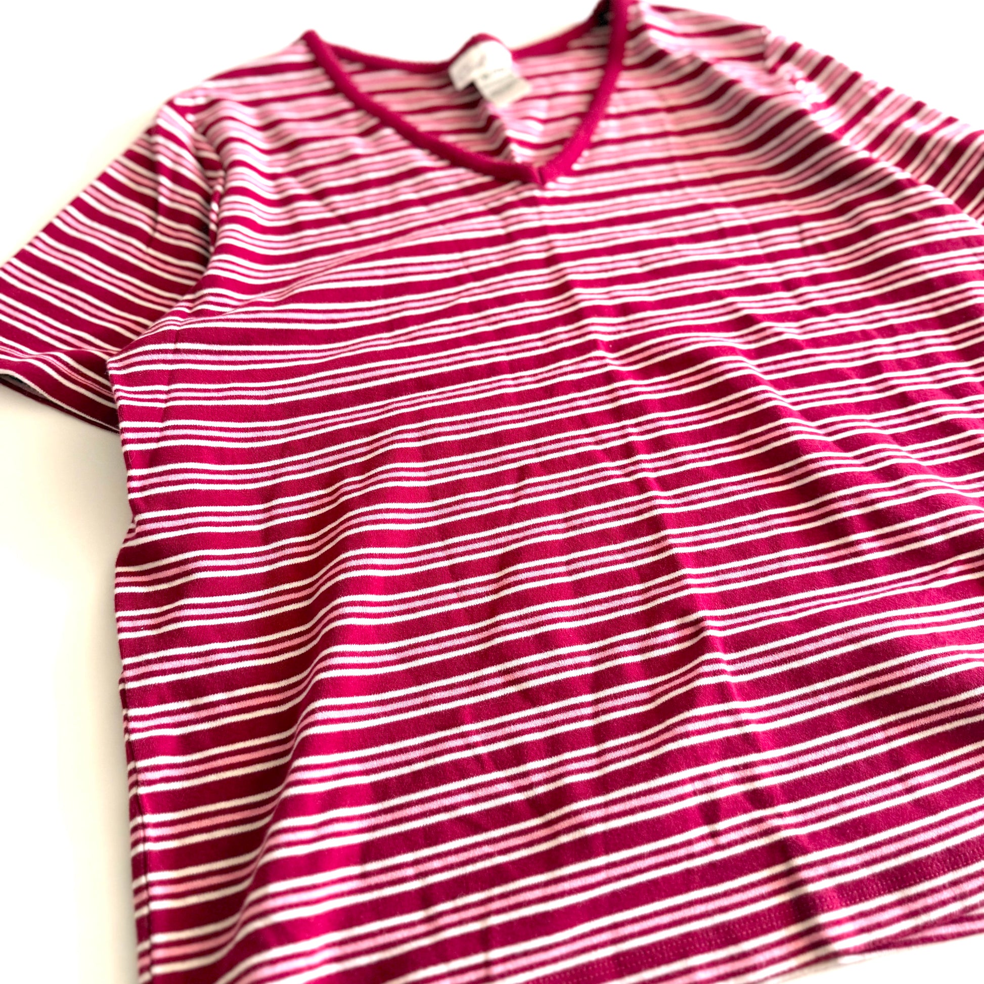 White, pink, and red striped t-shirt with a v-neck collar on a white backdrop. 