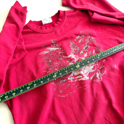 Bold pink sweatshirt / crewneck with a winter scene on the front  laid on a white backdrop - with a measuring tape laid out on it. 