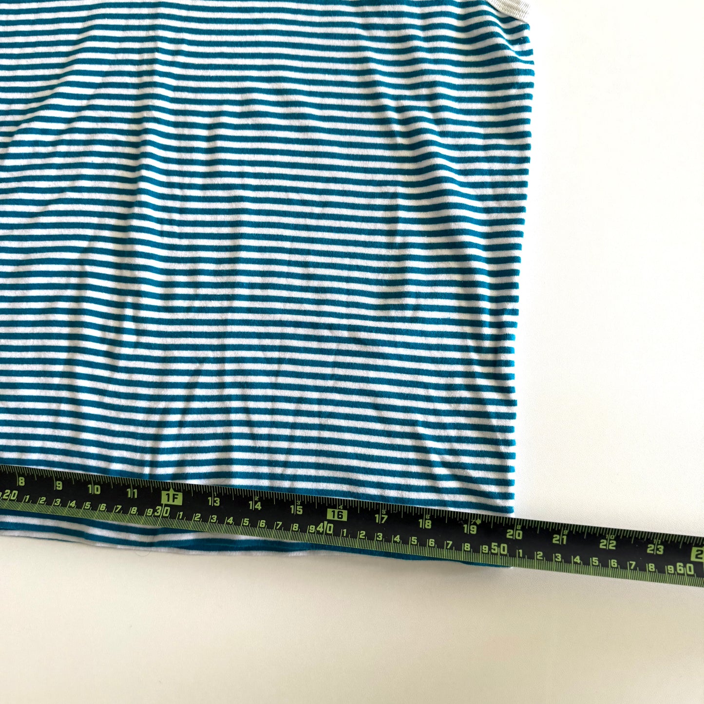 White and turquoise striped tank top with polo neckline, on a white backdrop and a measuring tape laid on top of it. 