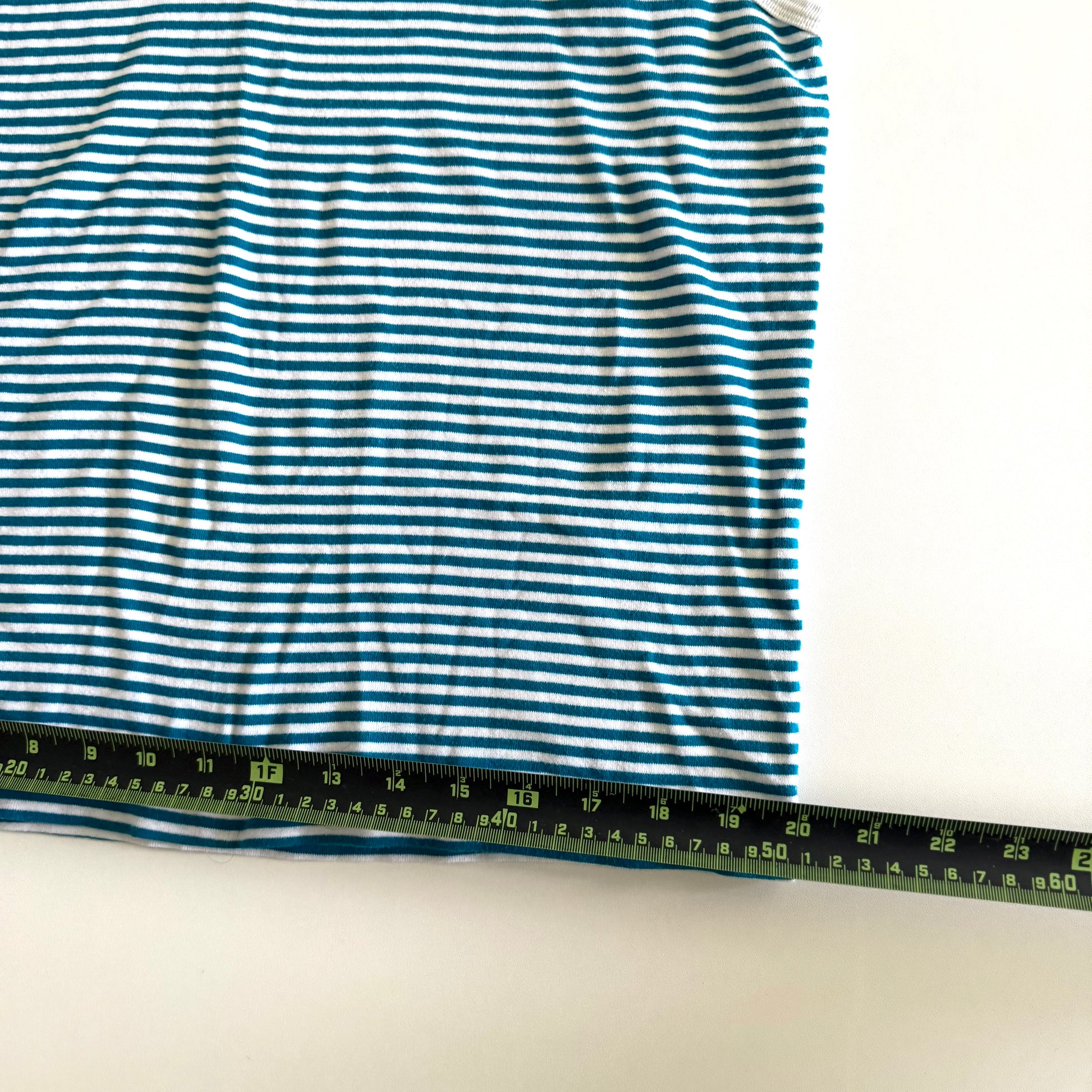 White and turquoise striped tank top with polo neckline, on a white backdrop and a measuring tape laid on top of it. 