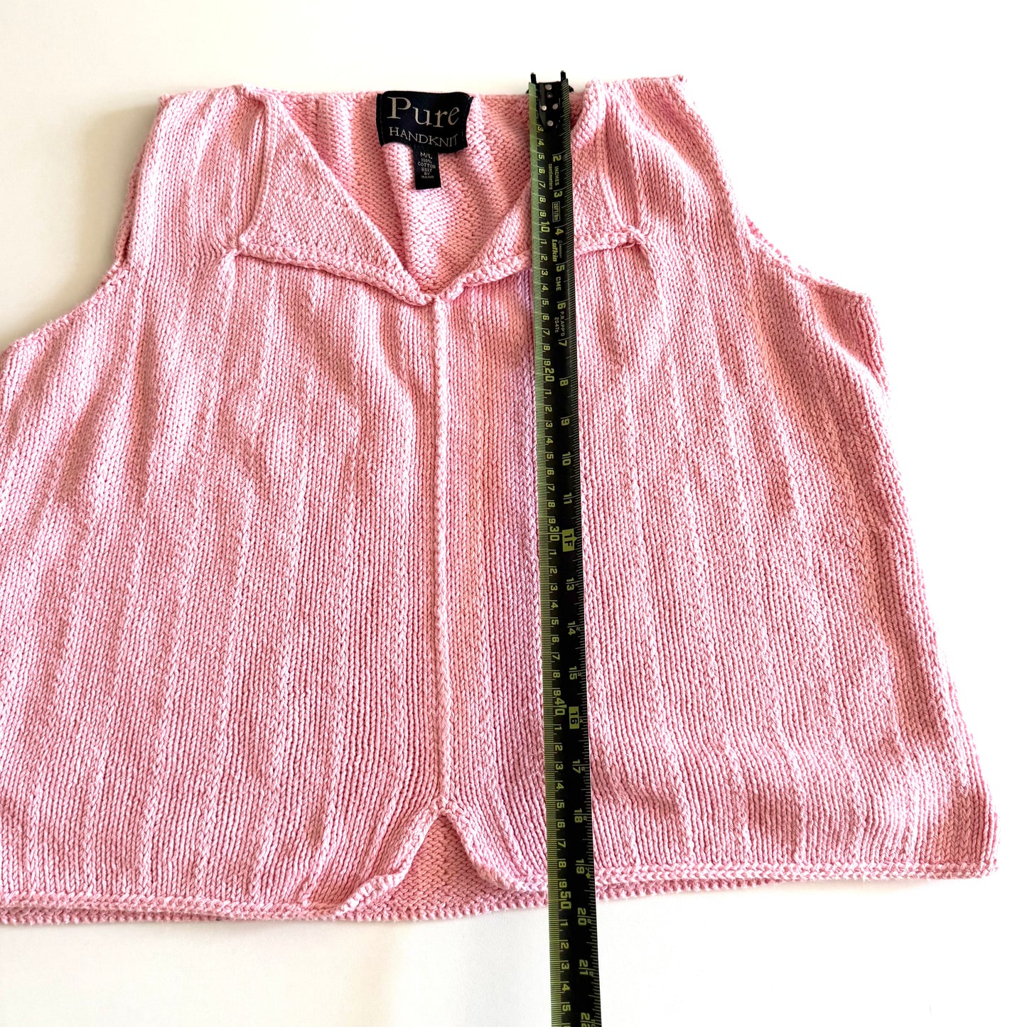 Light pink knit style tank top, with folded out collar opening on a white backdrop - with a measuring tape laid on top. 
