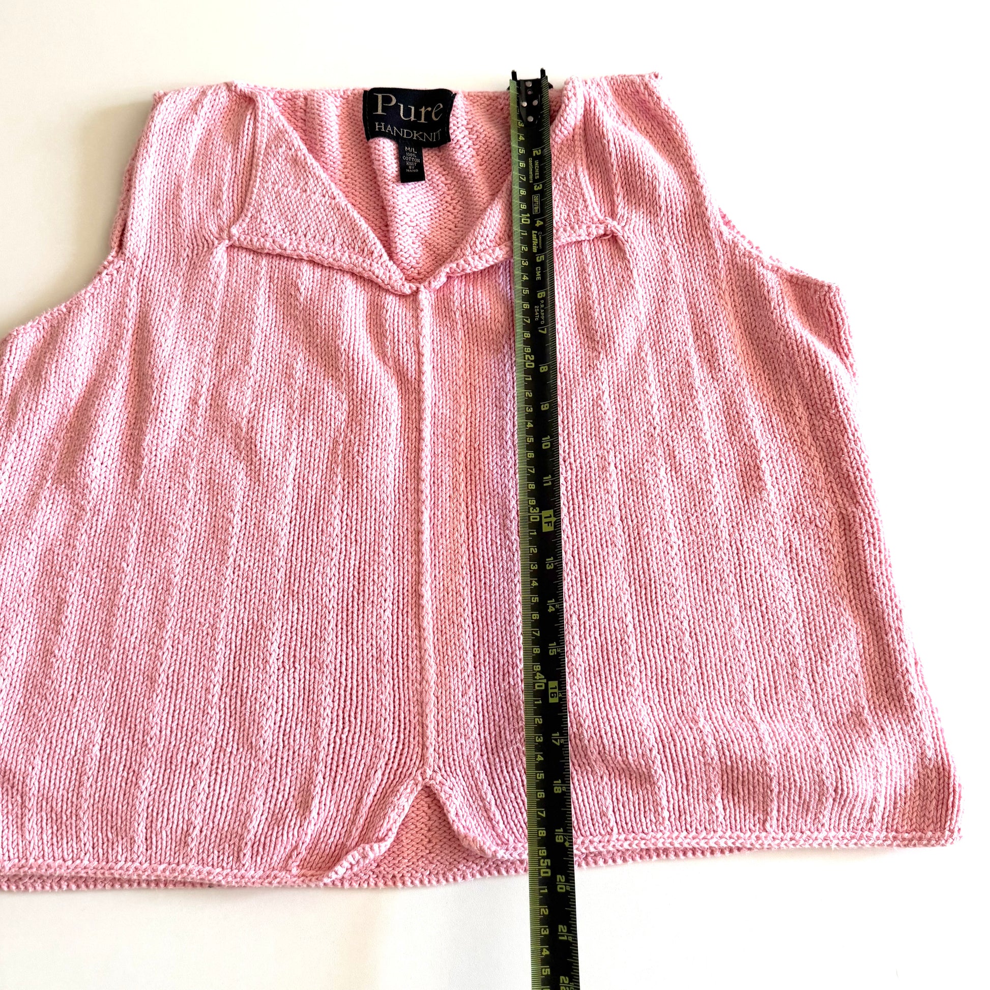 Light pink knit style tank top, with folded out collar opening on a white backdrop - with a measuring tape laid on top. 