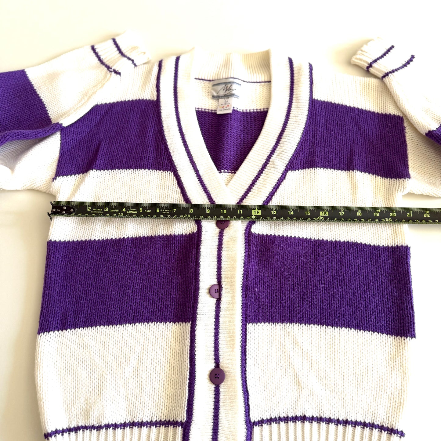 1990's preppy style - purple and white striped cardigan with a measuring tape on it on a white backdrop. 