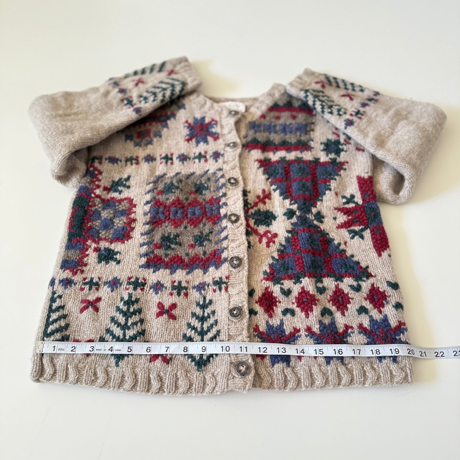 Knitted cardigan with geometric pattern and fluffy collar, measured against a white background.