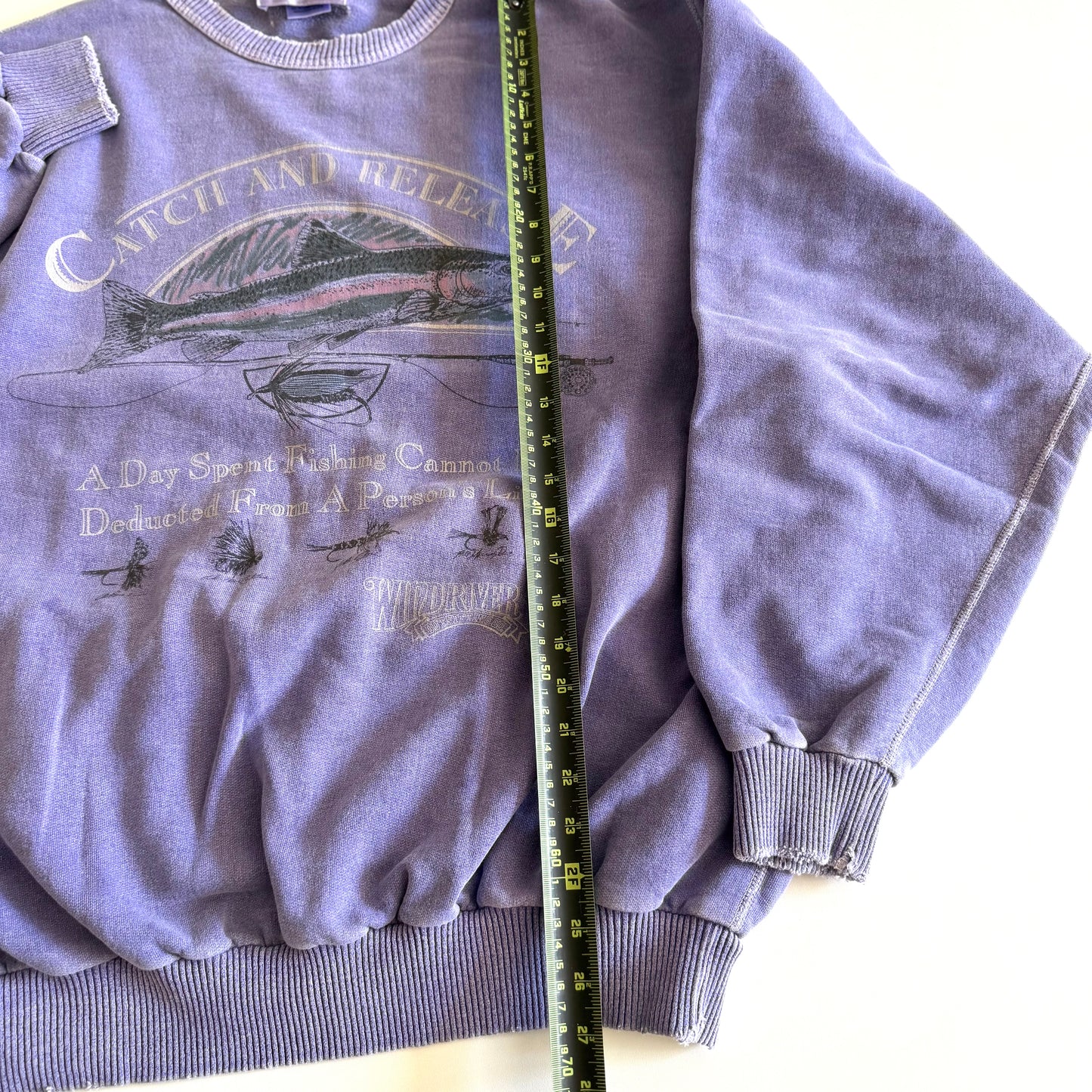 Light purple sweatshirt with fishing theme images and words on the front, on a white backdrop - with a measuring tape laid on it. 