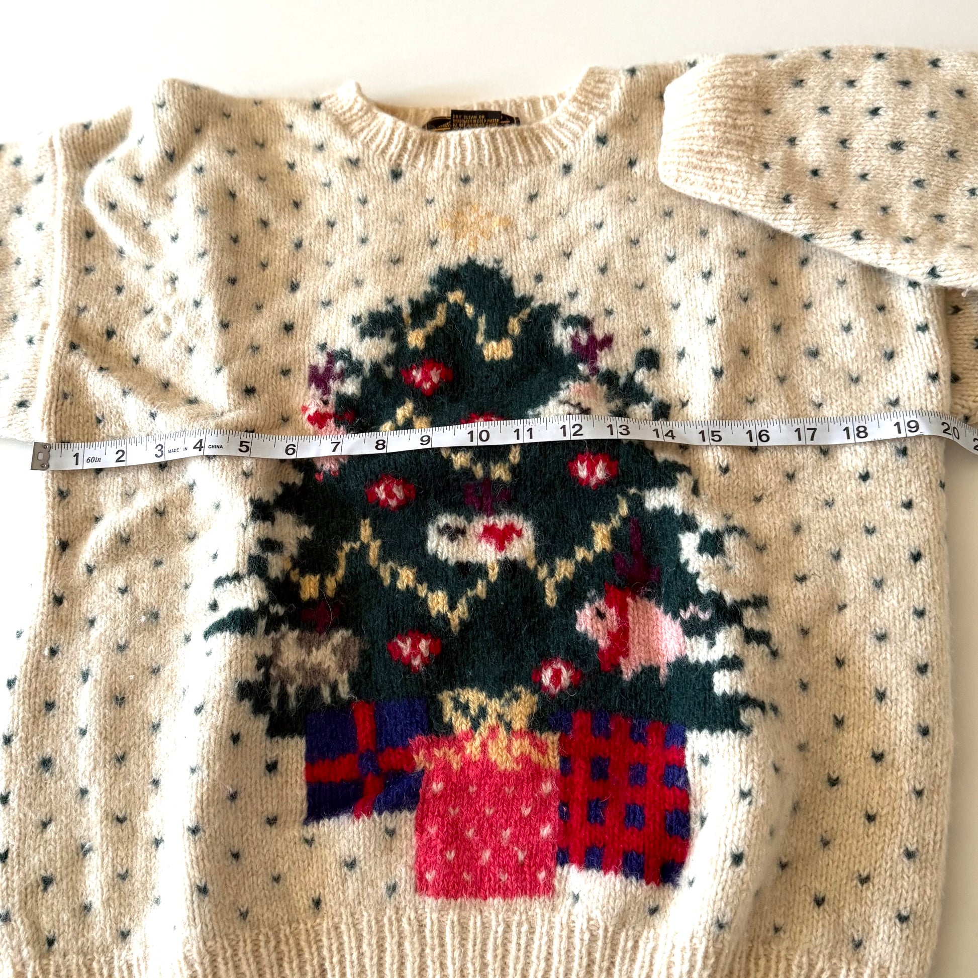 Beige sweater with a Christmas tree design and measuring tape for size reference.