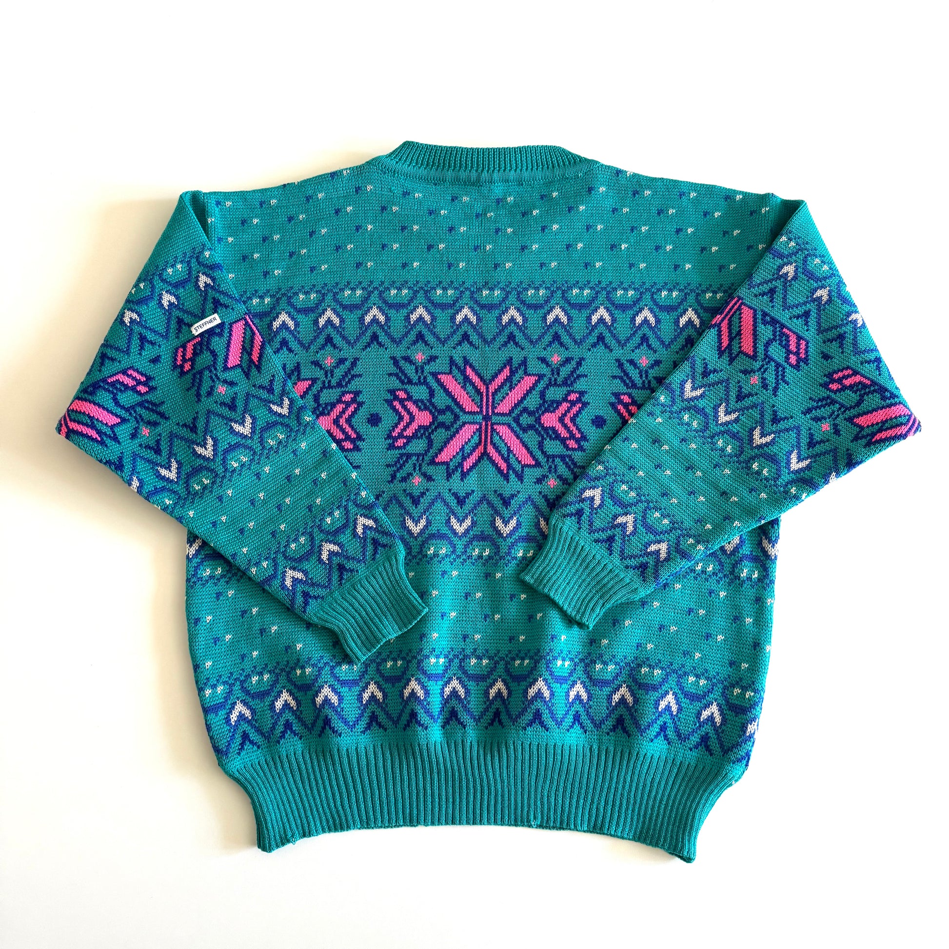 Backside of Teal and pink sweater with an aztec / snowflake adjacent style pattern, on a white background. 