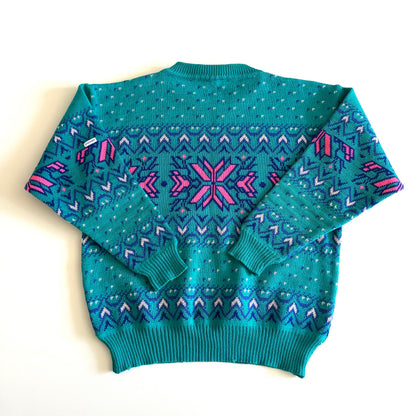 Backside of Teal and pink sweater with an aztec / snowflake adjacent style pattern, on a white background. 