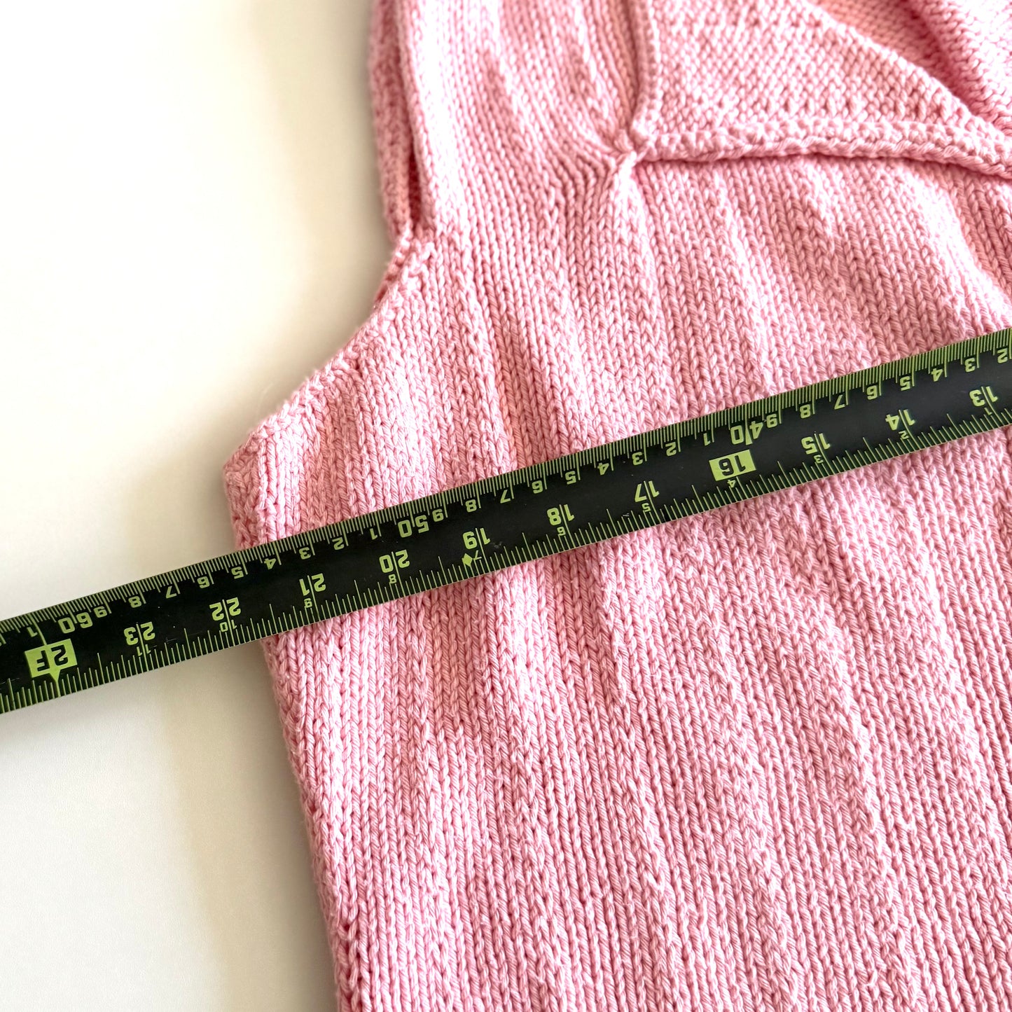 Light pink knit style tank top, with folded out collar opening on a white backdrop - with a measuring tape laid on top. 