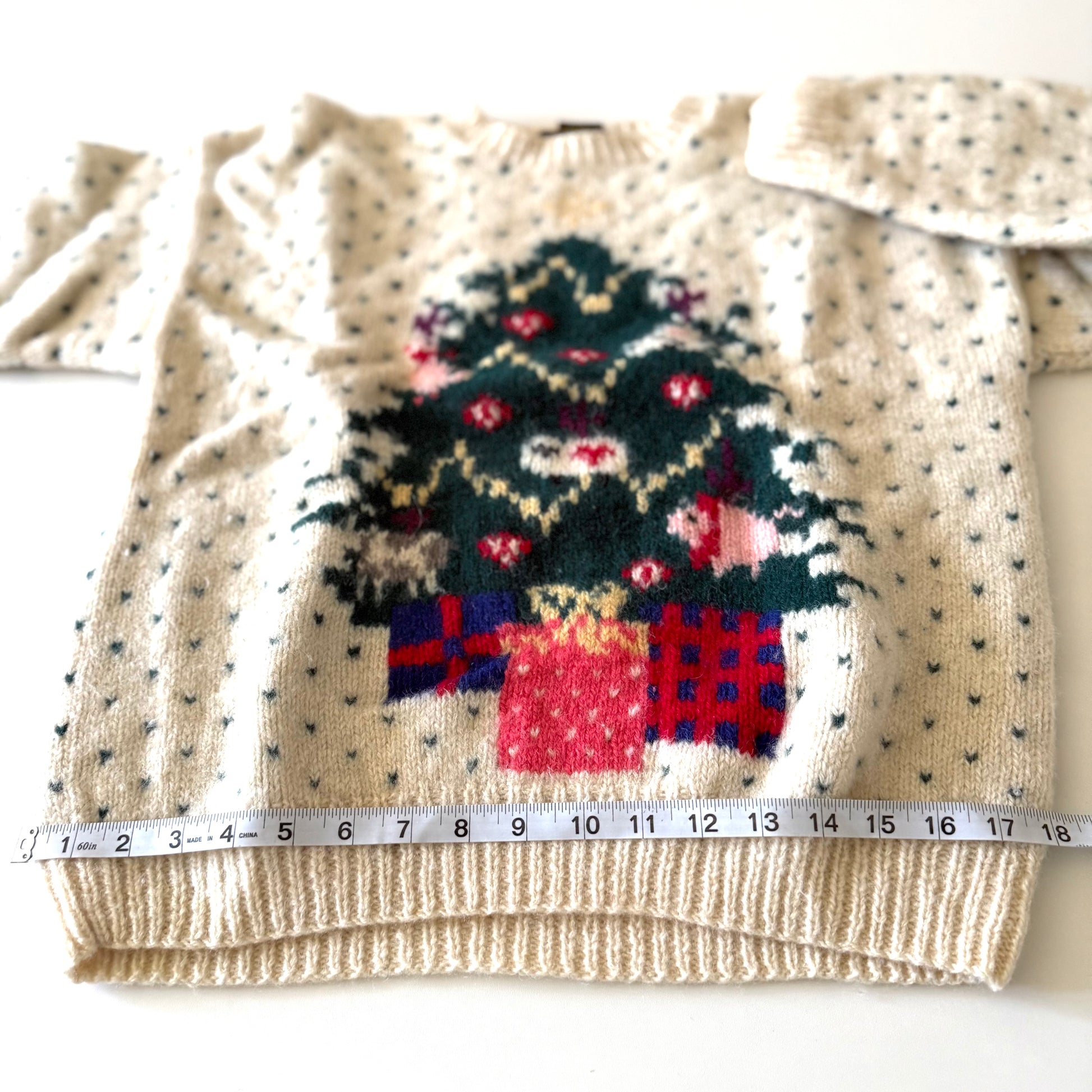 Knitted sweater with Christmas tree and presents design, measured against a ruler.