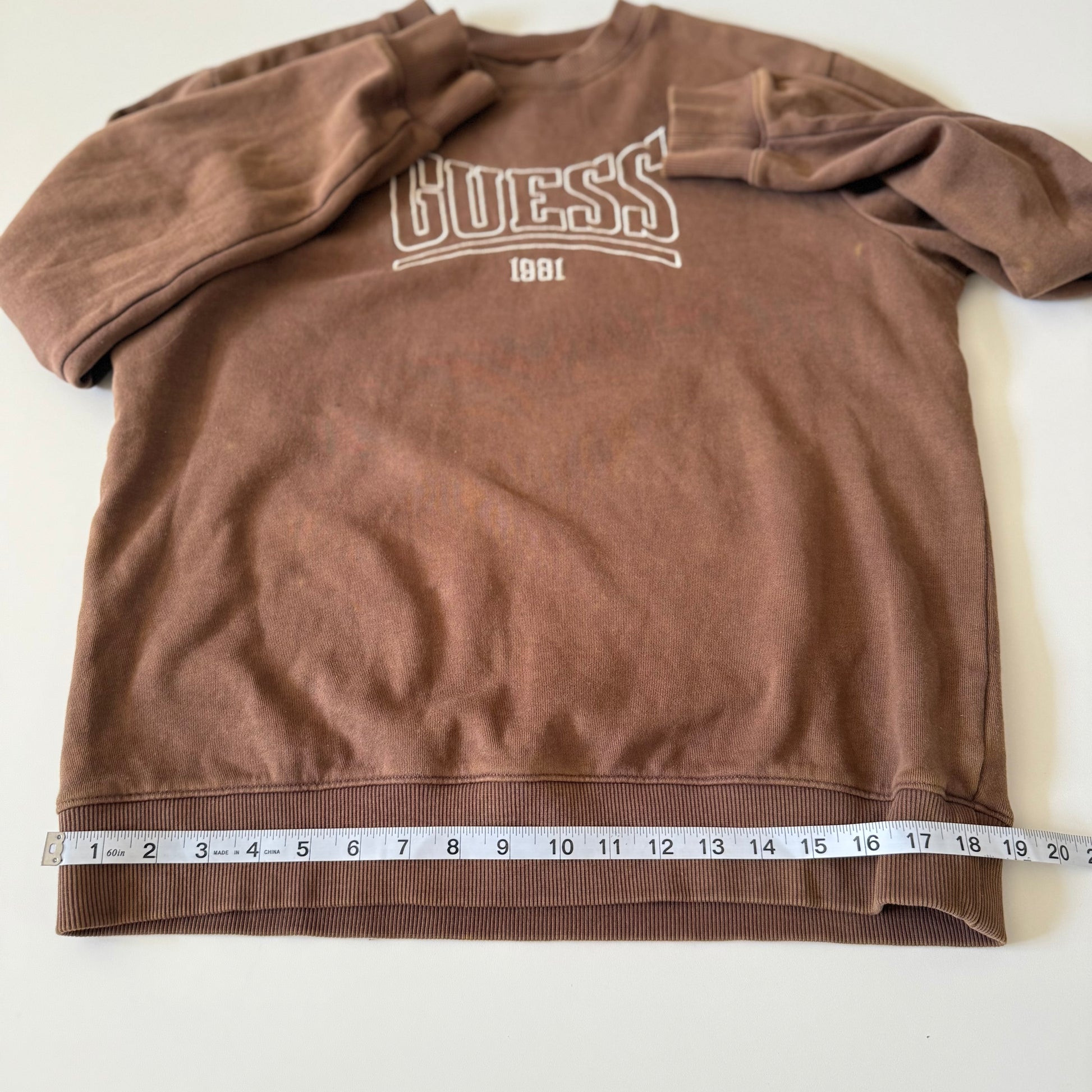 Brown Guess sweatshirt with a measuring tape at the bottom on a white background