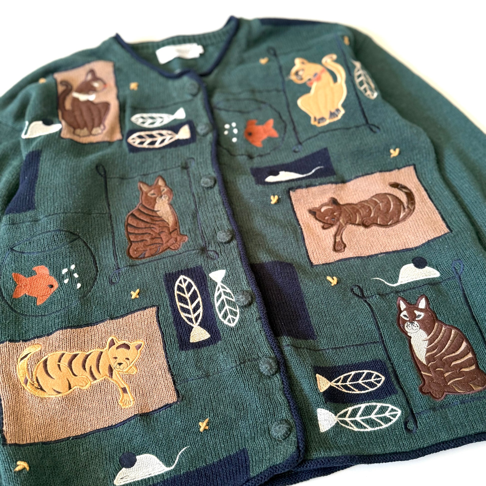 Green cardigan with cat-themed patches on a white background