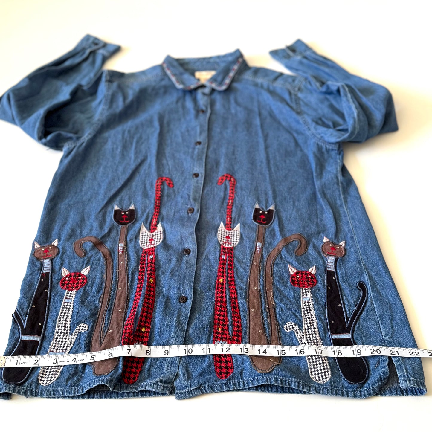 Blue denim shirt with cat appliqués on a white background