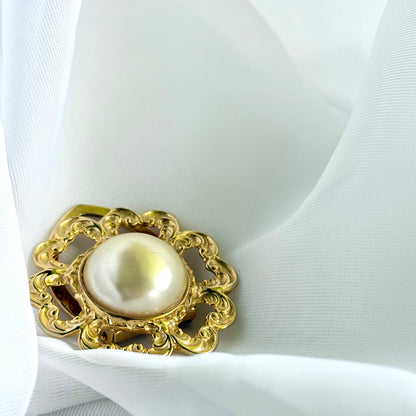 Gold brooch with a pearl on a white fabric background
