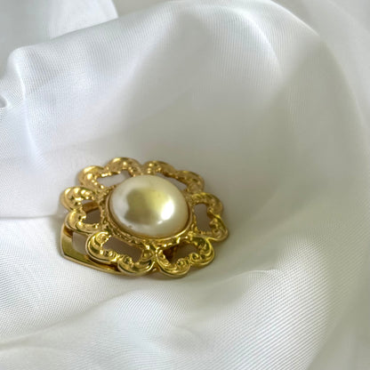 Gold brooch with a pearl on a white fabric background